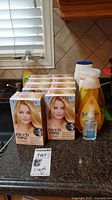 Photo of eight Clairol Nice'n Easy Cream hair color boxes in shade 8 Light Medium Blonde with model on front, along with three hair care bottles in background on a kitchen counter.