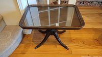 Square wood coffee table with glass top inset viewed from above and side showing claw feet and overall shape.
