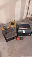Two plastic tackle boxes side by side on concrete floor with yellow device and two spherical floats in front