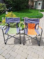 Two folding garden chairs side by side on a paved garden patio with lawn and garden in background.