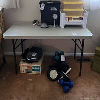 Folding table shown from front with items around and underneath it for scale and setting context.
