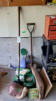 Overview of garden supplies including shovels, Scotts Turf Builder products, rolled yard waste bags, blue container with hand tools, and the green hand spreader in the shape of a hand.