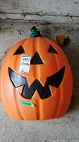 Front view of the large orange plastic Jack o Lantern with black facial features and green cord wrapped around the top