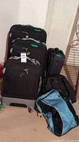 Photo showing all luggage and bags grouped together: three black Heys suitcases, Eddie Bauer suitcase, black backpack, blue and black duffel bag