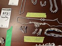 Photo of multiple rhinestone jewellery pieces on a wooden surface with green tape markers, showing necklaces, earrings, and a bracelet.