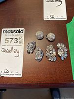 Photo showing six pairs of rhinestone clip-on costume jewelry earrings arranged on a wooden surface.