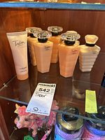 Lot of Lancôme Trésor lotions and perfume bottles displayed on a glass shelf, showing four peach color bottles with clear square caps and two tubes of body lotion.