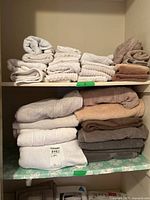 Two shelves in a linen closet holding neatly folded towels and linens in neutral colors like white, beige, brown, and gray