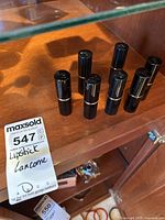 Six Lancôme lipsticks with caps on, black tubes with gold trim, standing on wooden surface.