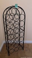 Metal wine rack showing full front view, black metal rack with circular bottle holders and four legs.