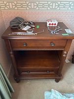 Front view of wood veneer nightstand with items on top and open shelf below, showing details of drawers and metal pulls.
