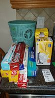 Photo showing the entire lot on kitchen counter with basket and all boxes and rolls of kitchen papers and bags.