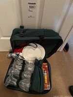 Photo of open soft sided picnic bag showing white plates, four clear plastic wine glasses, and packaged picnic cutlery inside