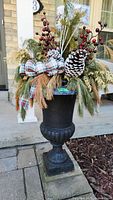Full view of black cast iron planter on stone slab, decorated with Christmas greenery, pine cones, red berries, and plaid ribbons.