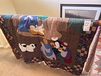 Photo showing quilt draped over railing, highlighting appliqued nativity figures including sheep and kneeling people in robes.