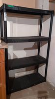 Front view of the black plastic shelving unit with four shelves against basement wall.