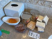Photo showing ceramic tissue box holder, ceramic soap dish with Pears soap, two scented candles, Ivory soap bars, and brown soap sponges arranged on countertop.
