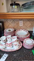 Full set of Stokes festive holly leaves Christmas dinnerware with cups, plates, bowls, creamer, sugar bowl, platter and serving bowl arranged on counter.