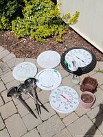 Outdoor solar garden stake lights, wall thermometers, decorative white garden plaques, and two small plant pots placed on patio stones near garden bed