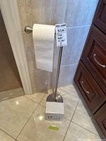 Freestanding brushed nickel toilet paper holder stand with toilet paper roll, square base, vertical pole, labeled with MaxSold tag