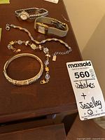Photo of the two watches and three bracelets together on wooden surface, includes a MaxSold tag with lot number 560