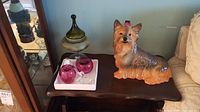 Image showing ceramic dog figure and two cranberry glass fruit on a wooden table next to a sofa.