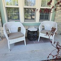 Photo showing two white wicker chairs with a rattan base table placed between them on a porch.