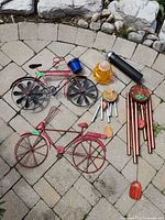 Lot items arranged on stone patio showing bicycles, wind chimes, bird feeder, wasp trap.