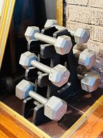 Front side view of steel hex dumbbells arranged on A-frame rack on wood floor near brick wall.