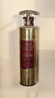 Front view of one brass antique fire extinguisher showing the red label with Quick Aid Fire Guard text