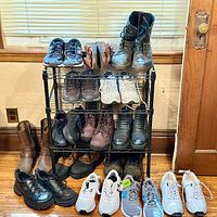 Black metal shoe rack with 13 pairs of men's boots and shoes arranged on and around it, primarily in size 8-9.