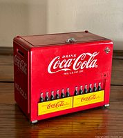 Front and side view showing Coca-Cola logo, 'ICE COLD' text, and miniature Coke bottles in yellow crates on red metal cooler-shaped music box.