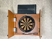 Dartboard cabinet open showing dartboard, darts, and attached scoreboard inside.