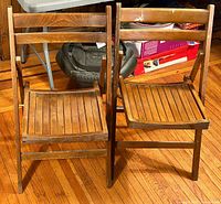 Pair of two folding wooden chairs positioned side by side on hardwood floor.