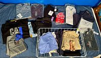 Overview of multiple men's clothing items including shirts, pants, and shorts, mostly new with tags, various colors and brands visible