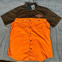 Front view of the orange and black Harley-Davidson buttondown shirt on hanger showing tags attached and logo on chest.