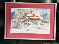 Framed watercolour painting showing a winter rustic cabin scene with snow and barren trees, matted with red and framed in light wood.