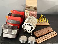 View showing four View-Master viewers: two red, one Joe Camel branded black, one in original box, multiple white reels on metal stand, two metal yo-yos, and two wooden games.