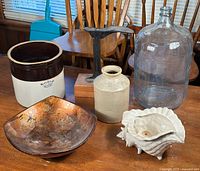 Full group of items displayed on table including antique shoe mold, two crocks, ceramic shell piece, and glass bottle.