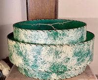 Photo showing the two-tiered circular lampshade with green and white textured fiberglass exterior and metal edge stitching.