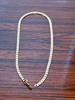 Full view of the necklace laid flat on wooden surface showing overall length and broken clasp.