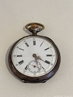 Front view of antique 800 silver pocket watch showing white porcelain face with Roman numerals, ornate hands, and inset seconds dial. Noticeable chip near center of face.