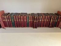 Shelf of approximately 32 leather-bound books by Collins with red and green spines and gilt lettering, flanked by slipcases
