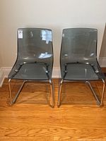 Front view of two smoky acrylic cantilever chairs with chrome tubular frames, placed on wood floor.