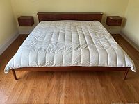Front elevation view of teak platform bed frame with headboard and white quilt on hardwood floor