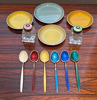 Overview of full lot: six multicolored enamel teaspoons, two shakers and four coasters on wood surface