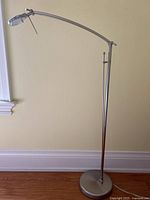 Full view of the modern metal floor lamp standing on hardwood floor with curved adjustable arm and circular LED light head.