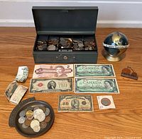 Overall arrangement showing cash box with coins, multiple paper bills, coin tray with loose coins, Penny Farthing model and globe bank.