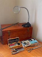 Magnifying glass on flexible neck and wooden box with metal tools arranged on table