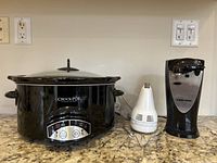 Photo of three small kitchen appliances on a granite counter: black Crock-Pot slow cooker with glass lid and control panel, white KitchenAid hand mixer with beaters, Black+Decker electric can opener in black and silver.